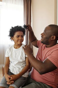 A father brushes his son's curly hair, showcasing love and parenthood indoors.